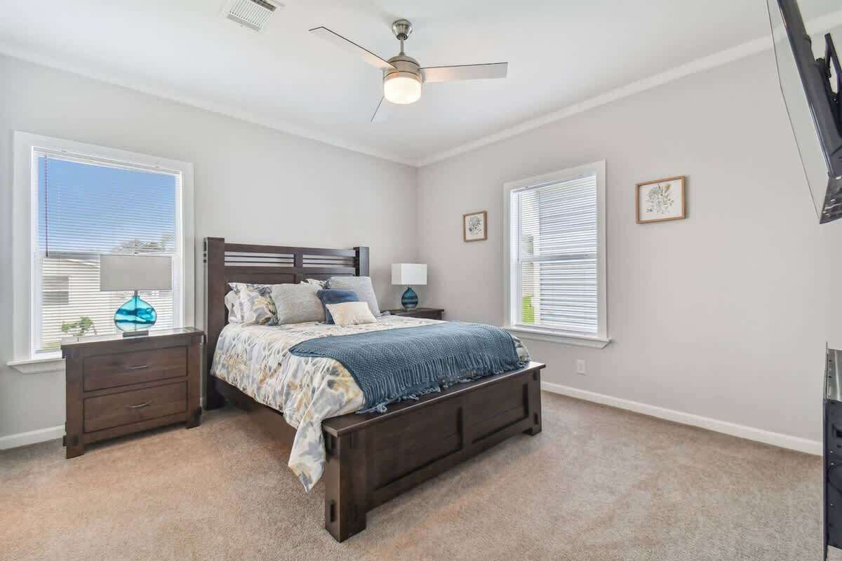 Un dormitorio con cama, mesitas de noche, ventilador de techo y ventanas con persianas.