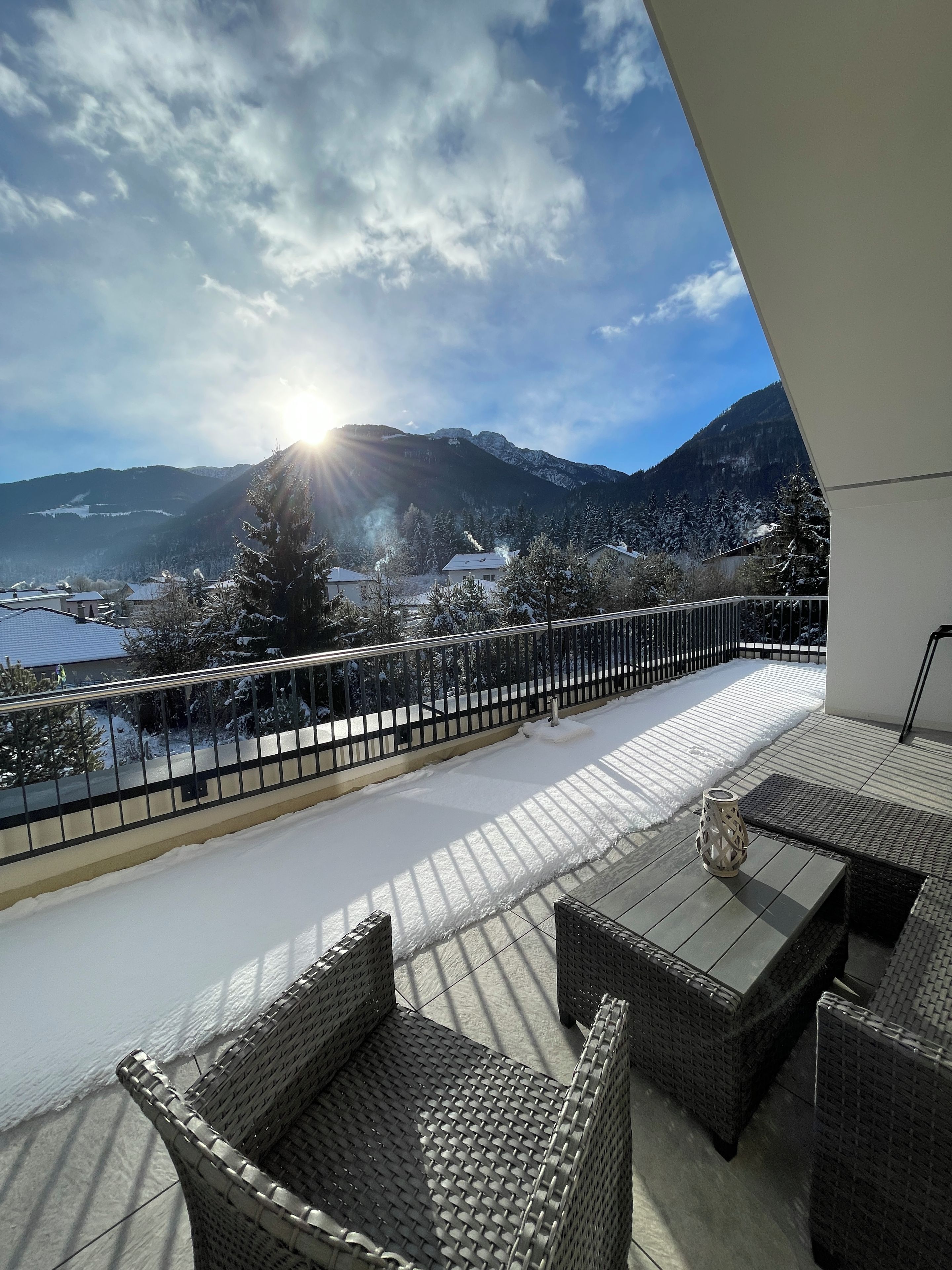 A balcony with wicker furniture, a view of snow-covered mountains, and a clear sky.