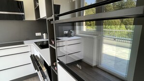 Una cucina moderna con mobili bianchi, un piano di lavoro nero e vista su un balcone con ringhiera.