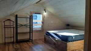 Ein kleines Schlafzimmer im Dachgeschoss mit schrägen Wänden, einem hölzernen Etagenbett, einem Oberlicht und einer Holzleiter.