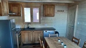 Eine kleine Küche mit Holzausstattung, inklusive Kühlschrank, Geschirrspüler und einem Esstisch mit Stühlen.