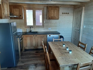 A compact kitchen with wooden cabinets, a refrigerator, a dishwasher, and a dining table with chairs.