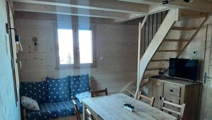 Ein gemütliches Blockhaus-Interieur mit einem Holzesstisch, einer Couch mit floralen Kissen, einer Treppe und einem Fernseher auf einem Holzschrank.