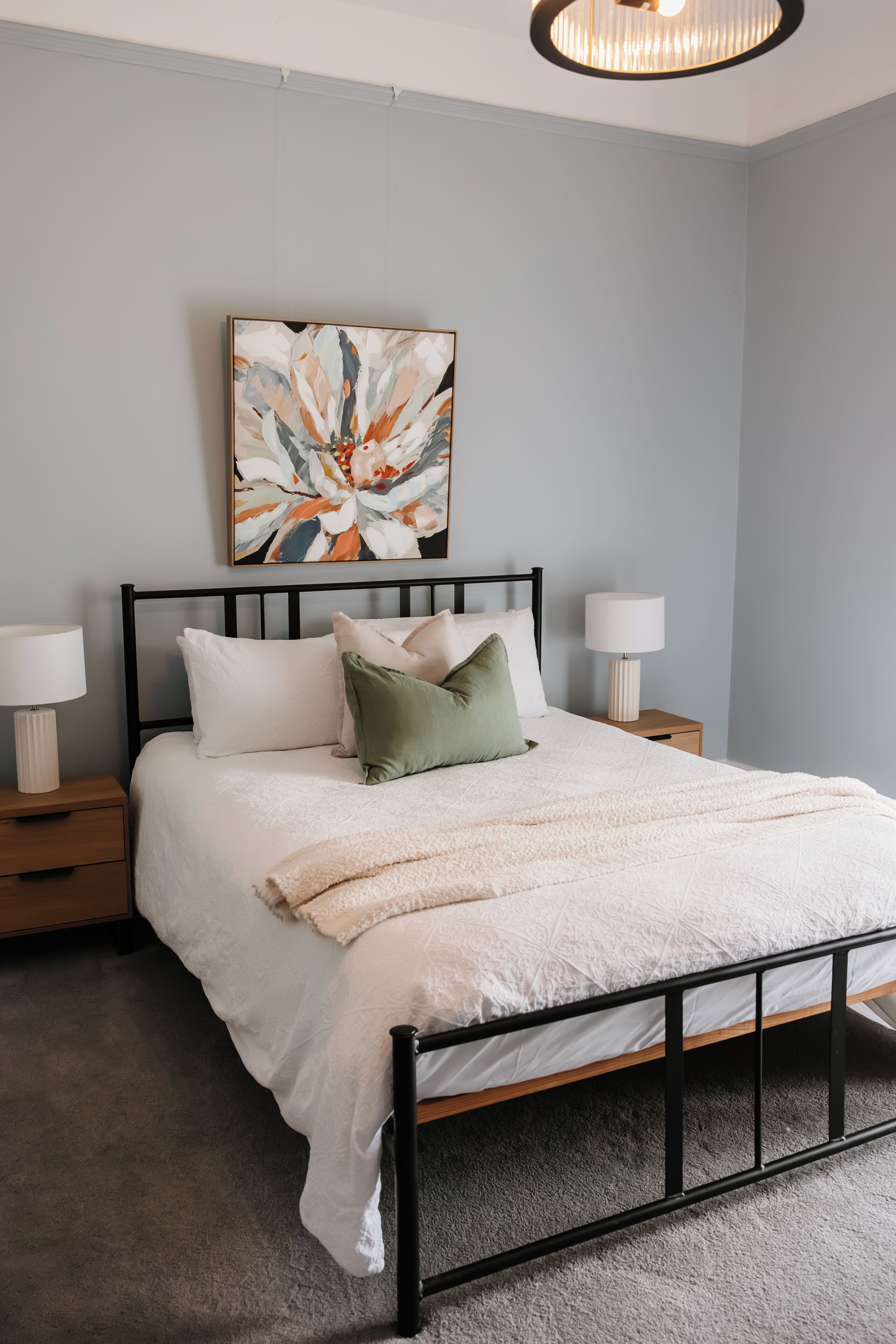 A bedroom with a bed, nightstands, a lamp, a painting, and a ceiling light fixture.