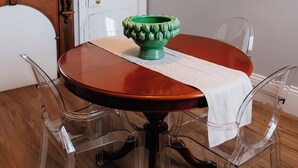 Un comedor con una mesa redonda de madera, sillas transparentes, un tazón verde sobre la mesa, una puerta blanca y un cuadro en la pared.