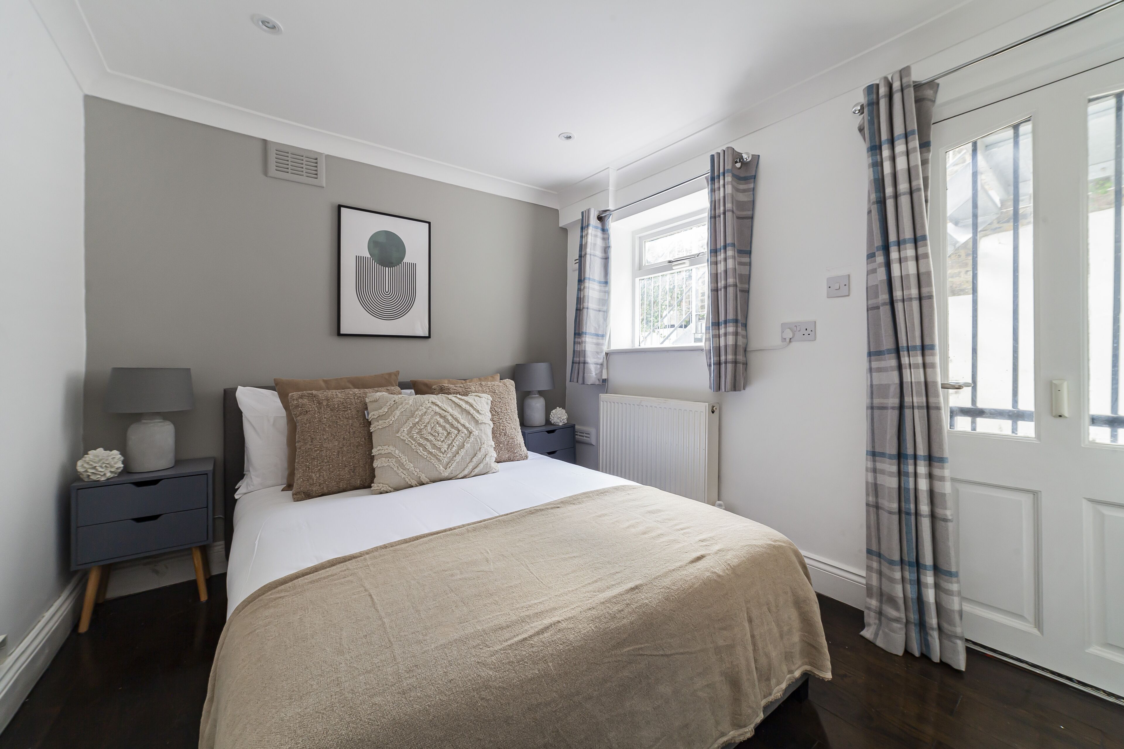 A bedroom with a large bed, a bedside table with a lamp, a radiator, and a window with curtains.