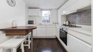 A modern kitchen with white cabinetry, a wooden table, a built-in oven, and a window with a view of the outside. - The Westbourne Villa (London)