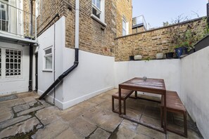 A narrow courtyard with a wooden bench and a white door. - The Westbourne Villa (London)