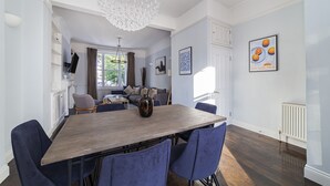 A dining area with a wooden table and blue chairs, a chandelier, and a framed picture on the wall. - The Westbourne Villa (London)