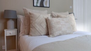 A neatly made bed with multiple pillows and a bedside table with a lamp. - The Westbourne Villa (London)