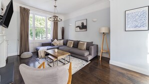 A modern living room with a grey sofa, a wooden coffee table, and a TV mounted on the wall. - The Westbourne Villa (London)