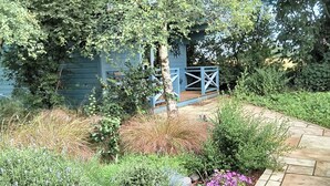Un jardín con un sendero de grava que lleva a una casa azul con una terraza de madera.