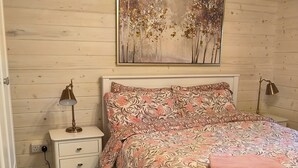 Un dormitorio con cama, mesita de noche, lámpara, un cuadro y alfombra estampada.