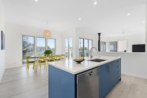 Uma cozinha moderna com uma ilha grande, uma área de refeições com cadeiras amarelas e grandes janelas com vista para o exterior.