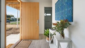 Et moderne interiør med en trædør, et hvidt konsolbord med planter, og en væg med blåt mønster.