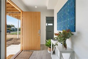 Um interior moderno com uma porta de madeira, um console branco com plantas e uma parede estampada em azul.