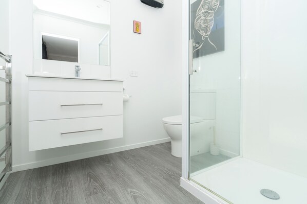 Un baño moderno con un tocador blanco, una cabina de ducha de vidrio y un inodoro.