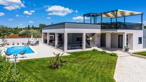 Una casa moderna su due piani con una zona relax esterna coperta, una piscina e un prato curato.