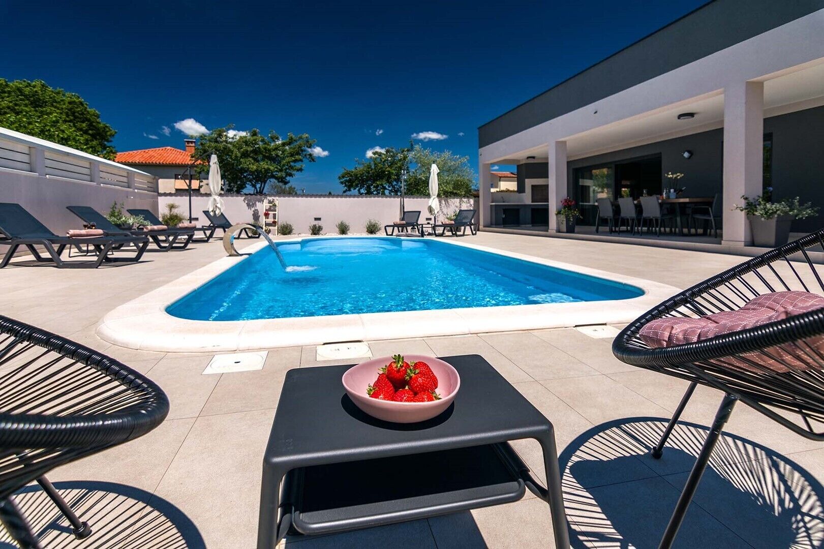 Une piscine avec des chaises longues et une table sur laquelle se trouve un saladier rempli de fraises.