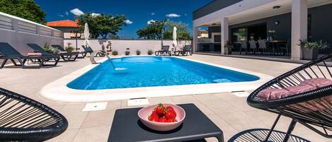 Une piscine avec des chaises longues et une table sur laquelle se trouve un saladier rempli de fraises.