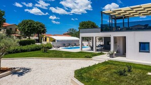 Una casa moderna con piscina, area relax esterna coperta e vista sulle case vicine.