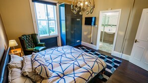 A bedroom with a bed, a chair, a TV, a wardrobe, and a bathroom visible through an open door. - Stylish One Bedroom Flat in Kensingston, London (London)