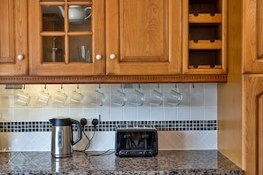 Kitchen area with wooden cabinetry and a geometric-patterned backsplash, featuring a kettle and toaster.