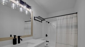 A bathroom with a white sink, black faucet, and a mirror above it. There is a shower curtain and a towel rack on the wall. - Condo near downtown Austin, close to Town Lake! (Austin)