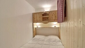 A small, cozy room with a single bed, wooden headboard, and a small shelf above the bed. - 250m from ski slopes, 4th floor, balcony, 26m², Méribel-Mottaret (Méribel - Les Allues)