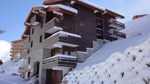 A multi-story building with balconies and a stone base, surrounded by snow. - 250m from ski slopes, 4th floor, balcony, 26m², Méribel-Mottaret (Méribel - Les Allues)