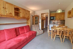 A cozy living area with a red sofa, a plaid armchair, and a wooden dining table with chairs. - 250m from ski slopes, 4th floor, balcony, 26m², Méribel-Mottaret (Méribel - Les Allues)