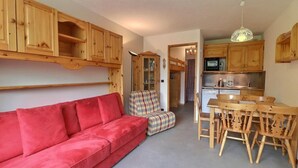 A cozy living room with a red sofa, a plaid armchair, and a wooden dining table with chairs. - 250m from ski slopes, 4th floor, balcony, 26m², Méribel-Mottaret (Méribel - Les Allues)