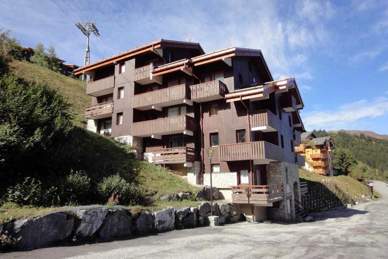 A multi-story hotel with balconies, set against a hillside backdrop.
