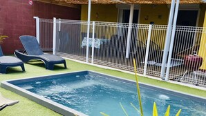 Una piscina rectangular con una valla blanca, rodeada de césped artificial verde y dos sillas de descanso.