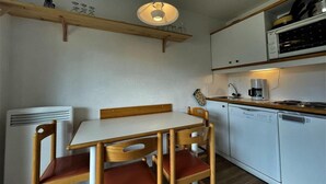Cocina compacta con una mesa blanca, sillas de madera, lámpara colgante y muebles de cocina blancos.