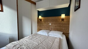 A bedroom with a bed, wooden headboard, two wall-mounted lamps, and a white door. - 130m from ski slopes, 8th floor, view ski slopes, balcony, ski locker, 33m², Méribel-Mottaret (Méribel - Les Allues)