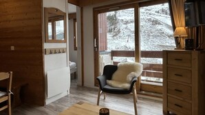 A cozy room with a wooden floor, a chair with a fur throw, a wooden dresser, and a window with a snowy view. - 130m from ski slopes, 8th floor, view ski slopes, balcony, ski locker, 33m², Méribel-Mottaret (Méribel - Les Allues)