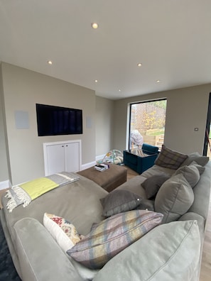 Relax in this stylish living room with a large sofa, flat-screen TV, and a window offering a view of the outdoors.