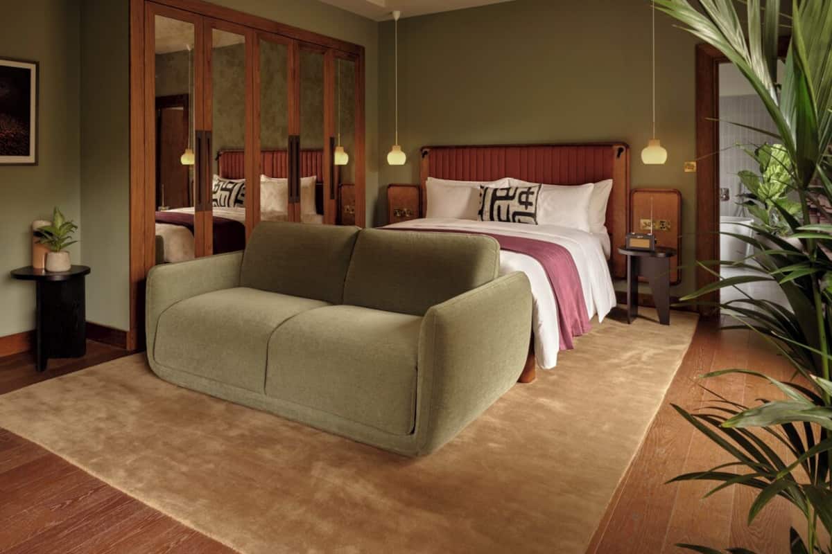 Un dormitorio con una cama grande, un sofá verde, un armario de madera y una mesita con una planta.