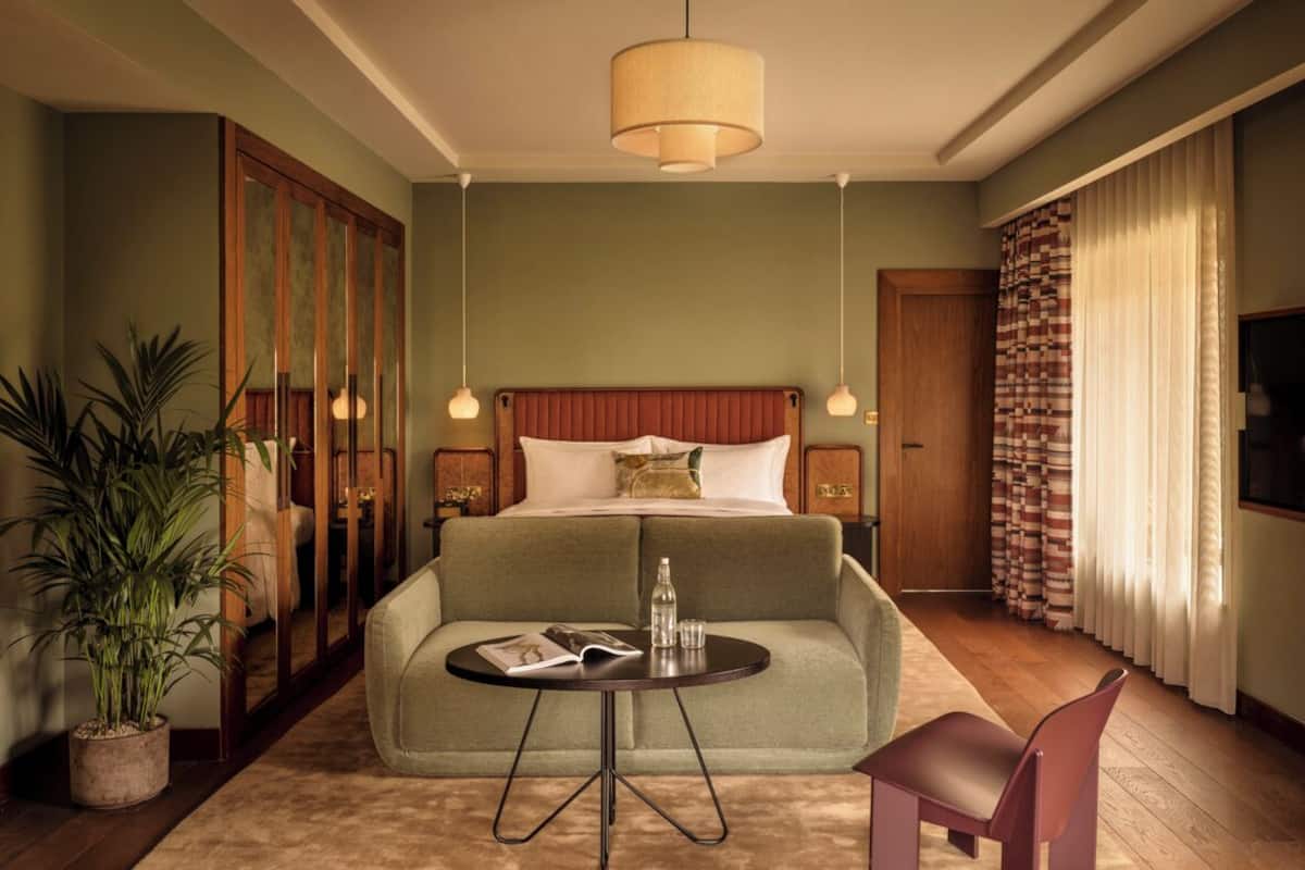 Una habitación de hotel con una cama, una mesa redonda, una silla, una planta en maceta y un espejo grande.