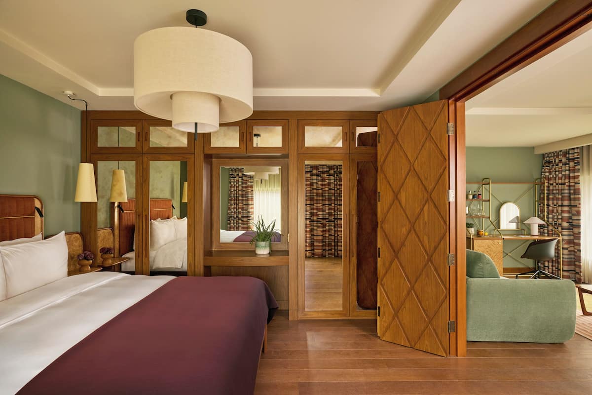 Una habitación de hotel con una cama grande, un escritorio con una silla, un armario y un espejo.