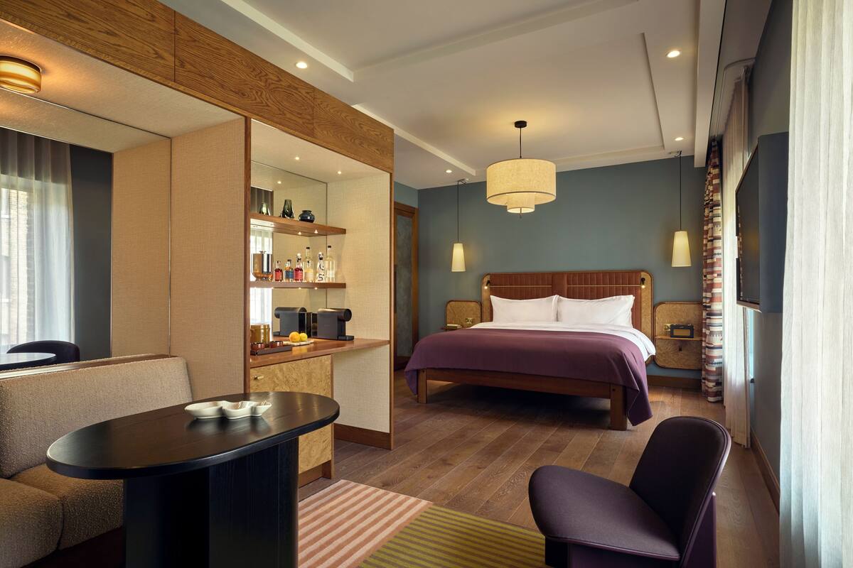 Una habitación de hotel con una cama, un escritorio, una silla, un televisor y un minibar.