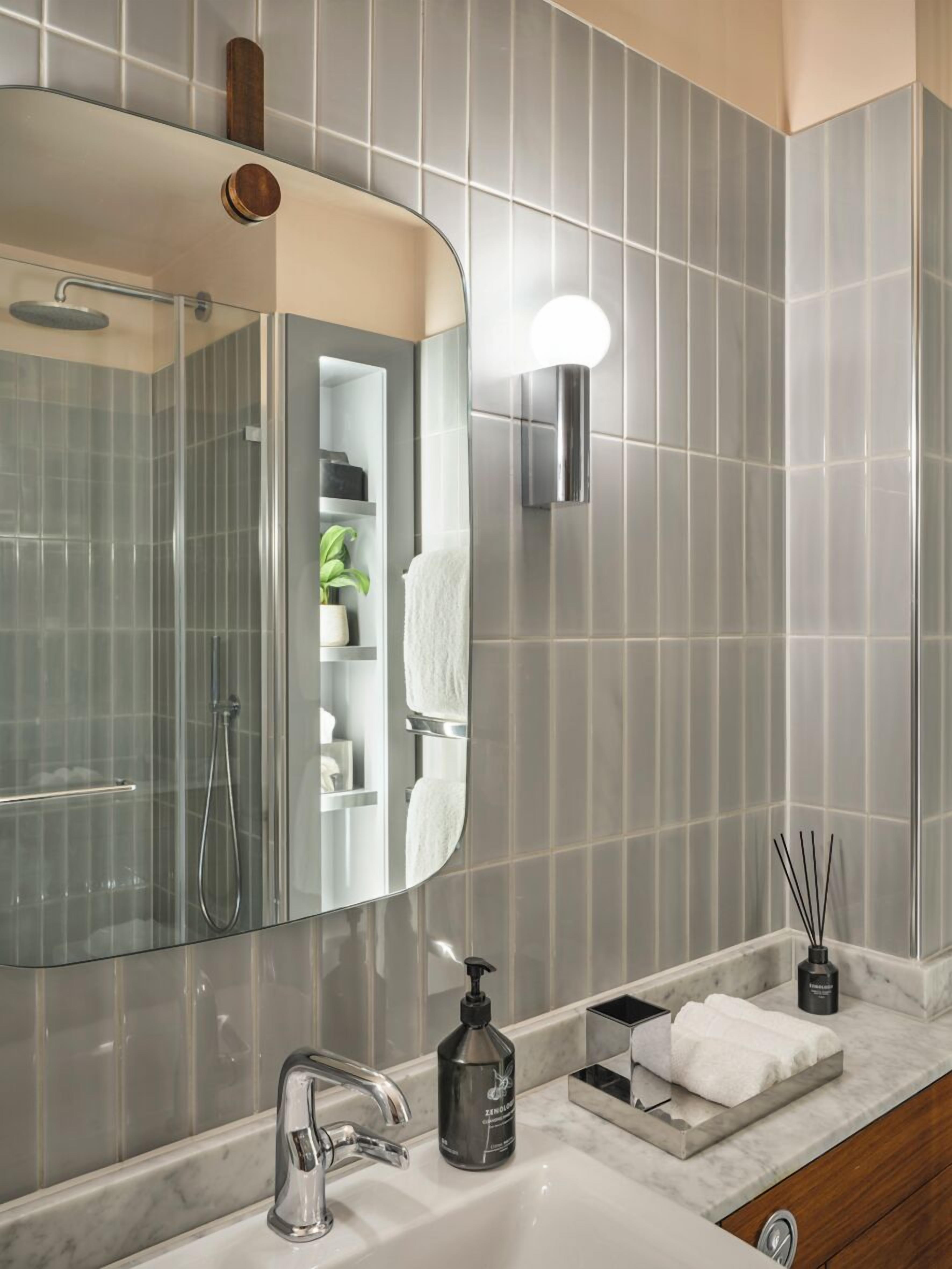 Une salle de bain moderne dotée d’un grand miroir, d’une douche à parois de verre, d’un comptoir en marbre et d’un luminaire fixé au mur.