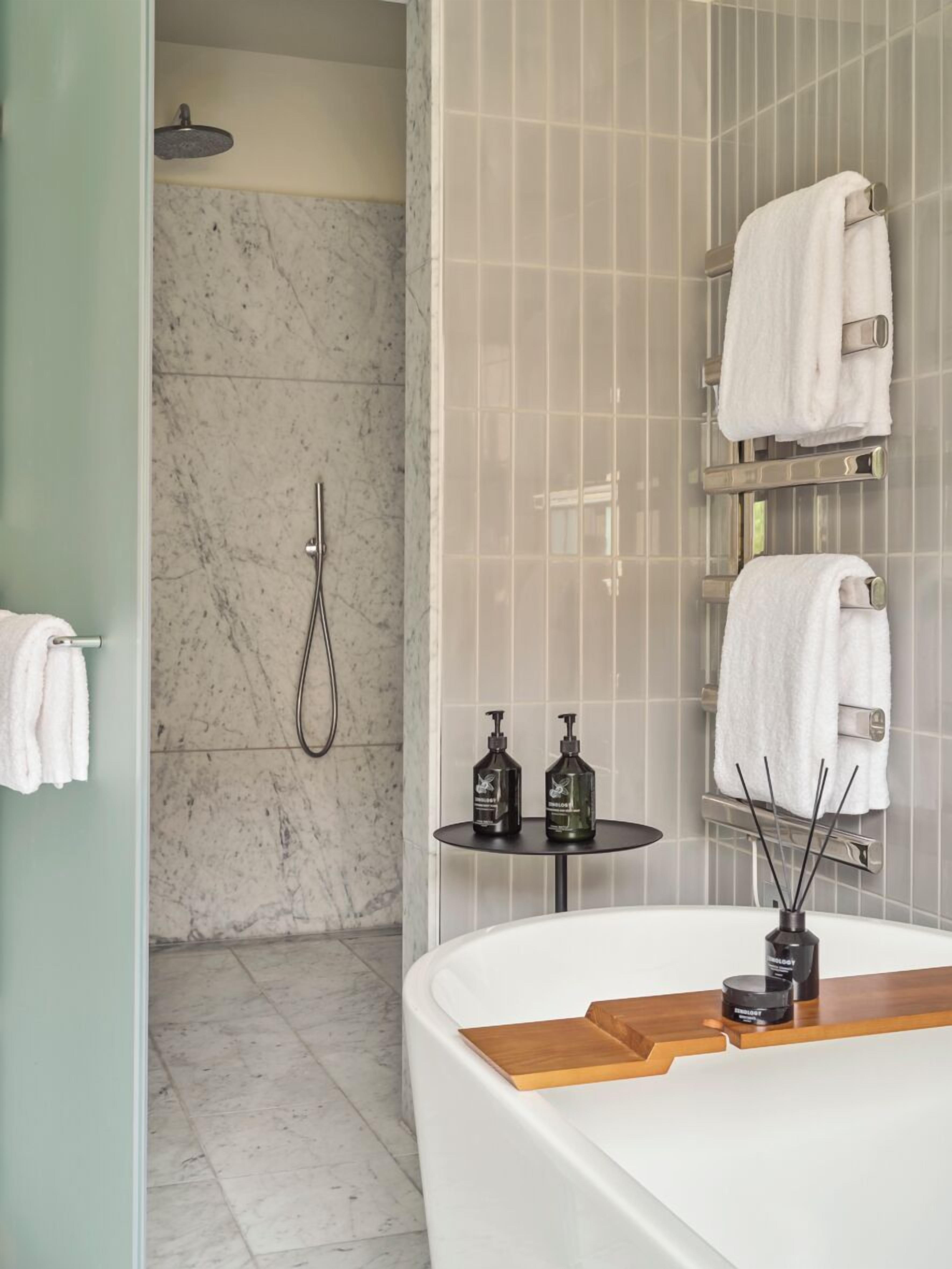 Ein modernes Badezimmer mit einer Marmordusche, einer großzügigen Badewanne und einem kleinen runden Tisch mit Pflegeprodukten.