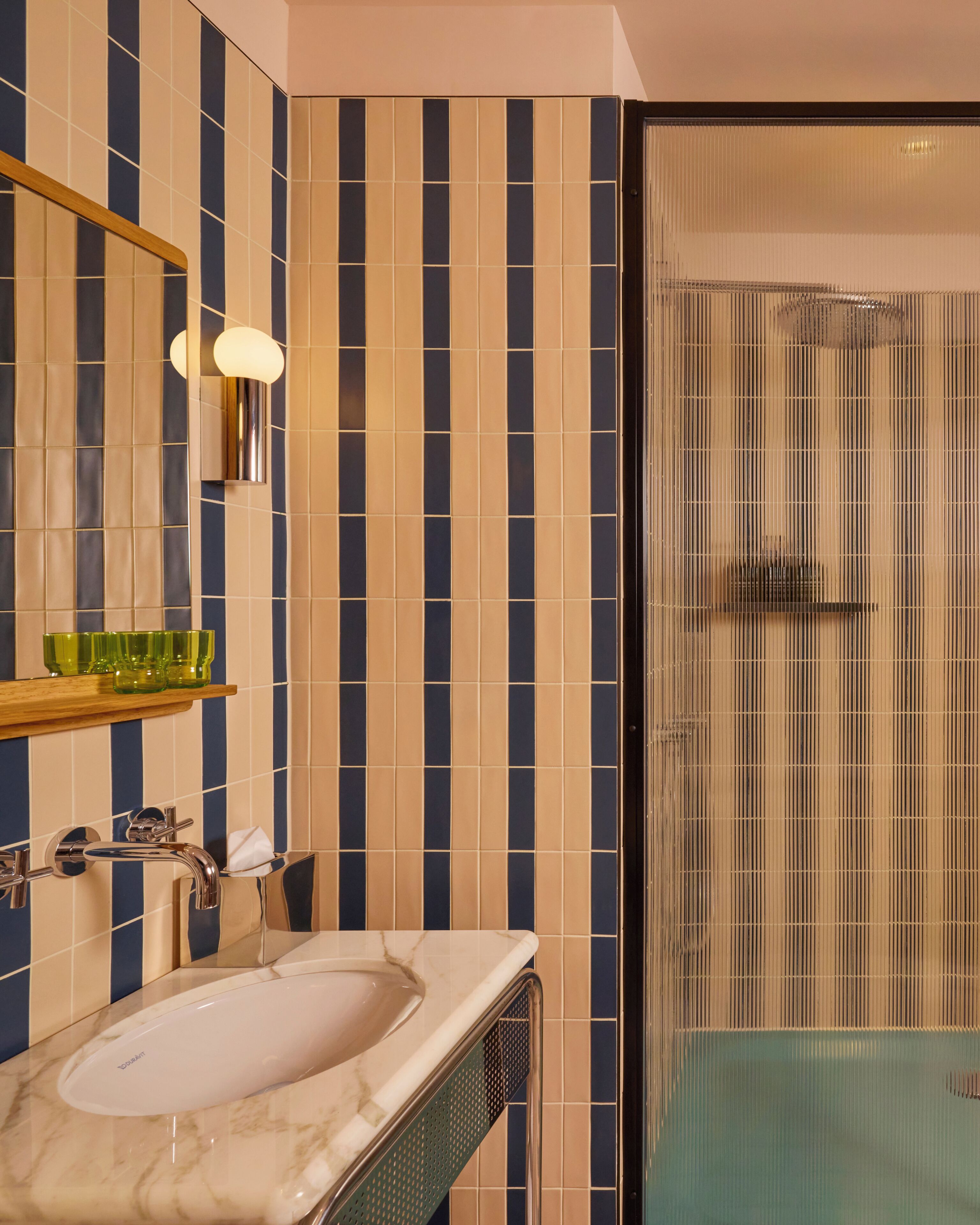 A bathroom with striped tile walls, a marble sink, a mirror, and a glass shower enclosure.