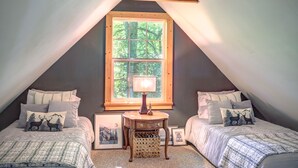 A cozy attic bedroom with two beds, a small table, and a window with a view of trees. - Visit #mytreetophideaway located in Banner Elk, NC, nestled high in the trees.  (Banner Elk)