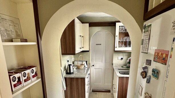 A narrow kitchen with a wooden cabinet, a white door, and a refrigerator with magnets.