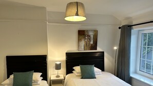 A hotel room with two beds, a nightstand with a lamp, a painting on the wall, and a window with curtains.