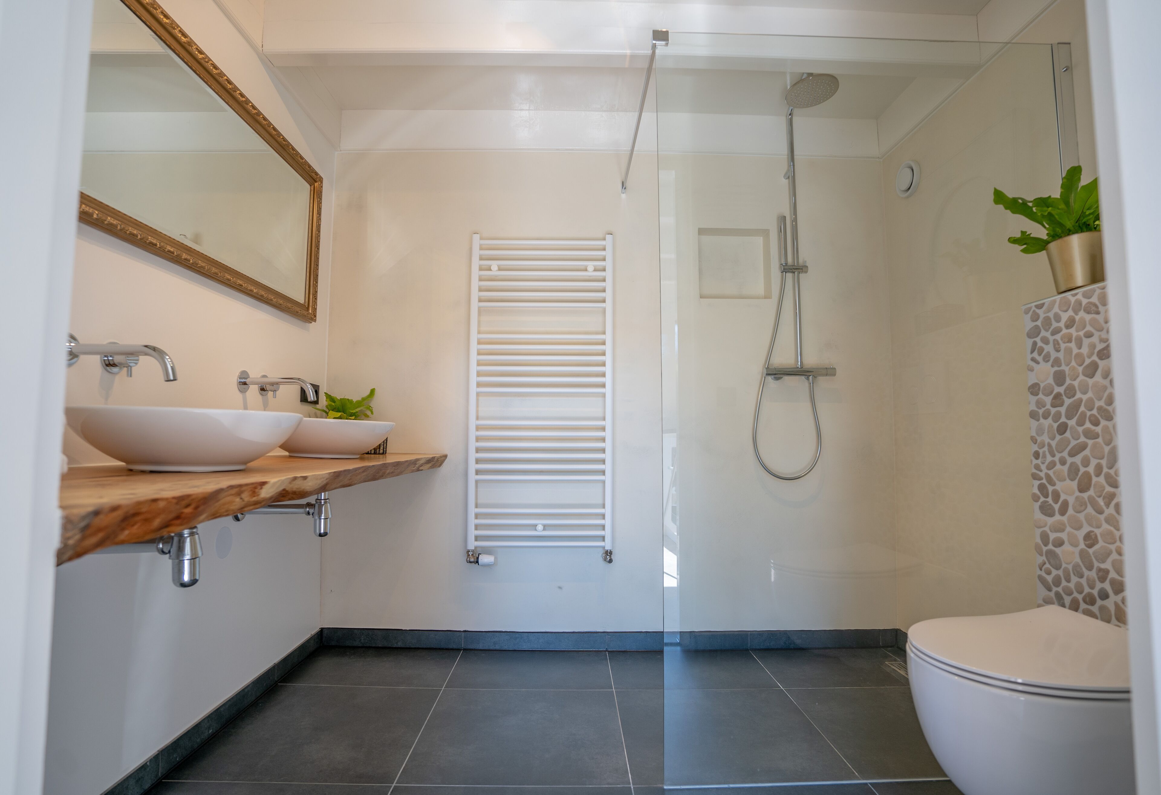 Un baño moderno con tocador de madera, dos lavamanos, un espejo, ducha e inodoro.