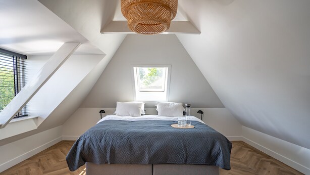 A bedroom with a sloped ceiling, a skylight, a bed with a blue quilt, and a woven light fixture. - Neu:wunderschöne und Preiswerte Ferienwohnung mit Jedem Komfort (Westhoek)